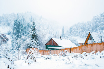 Winter village at the foot of the snowy mountains in winter fairy tale during snowfall
