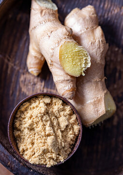 Ginger powder in a metal bowl and ginger roots