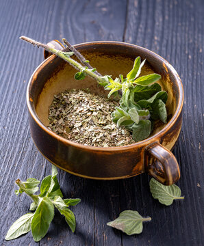 Chopped dried oregano placed in a ceramic bowl next to fresh oregano leaves