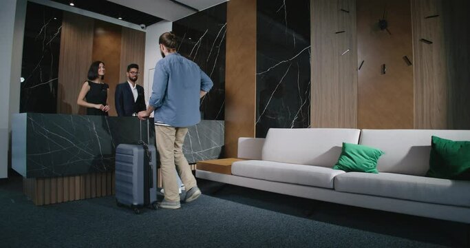 Energetic lovely people heading to hotel's front desk area, where male and female employees waiting to greet visitors. Young, experienced receptionists helping guests check in. Modern hotel concept.
