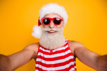 Photo of positive funky senior guy dressed christmas swimwear hat glasses recording video vlogging isolated yellow color background