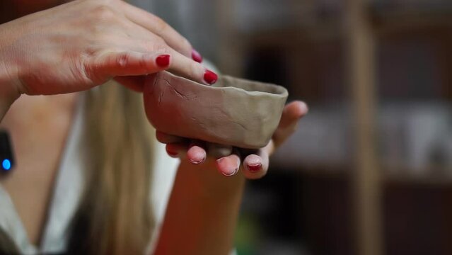 Woman holds with her hands and red manicure and forms a gray clay bowl for pottery. Crafting in the workshop, that illustrates the concept of home creativity, hobby and art