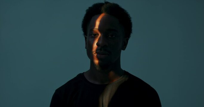 Abstract concept. African american dark skinned male man looking to the side turning head straight to camera looking directly catching light in dark studio.