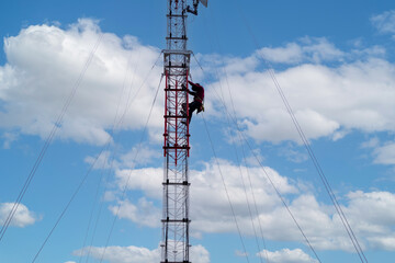 Electrician climbing on telecommunication tower Antenna with safety belt at summer sky.