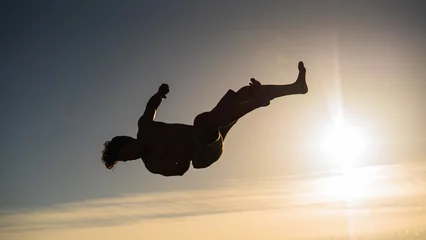 Foto op Plexiglas athletic young guy silhouette backflip in sunset © iago