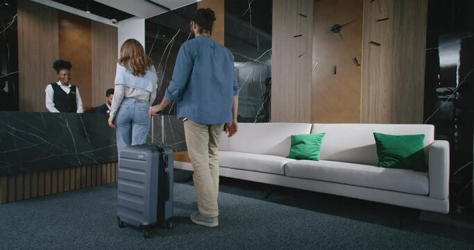 Lovely beautiful couple walking to hotel's reception desk where male and female receptionists waiting to greet visitors. Professional experienced nice hotel workers helping guests check in.