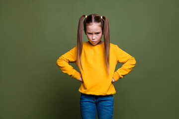 Portrait of offended small kid with tails hairstyle dressed yellow sweatshirt staring arms on waist...