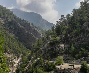 Fototapeta na wymiar Panoramic view of the Goynyuk Canyon. A small mountain stream runs through a wide rocky gorge. The steep slopes are covered with Mediterranean forest. A recreation area area by the road.