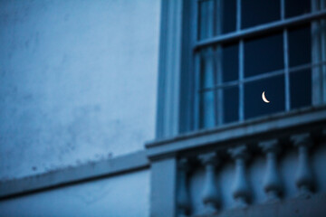 reflection of crescent moon in old fashioned window pane within an old mansion building 