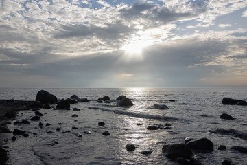 Fototapeta na wymiar Steine, Sonnenstrahlen und Wolken am Meer, Trauerkarte, Abschied