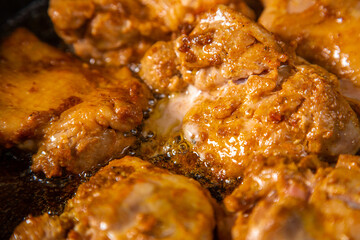 Chicken pieces in a sauce with spices are fried in a frying pan.