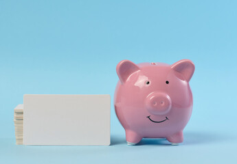 A pink ceramic piggy bank and a stack of white business cards on a blue background