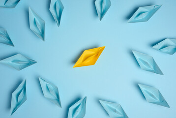 A group of blue paper boats surrounded one yellow boat, the concept of bullying, search for compromise. - obrazy, fototapety, plakaty