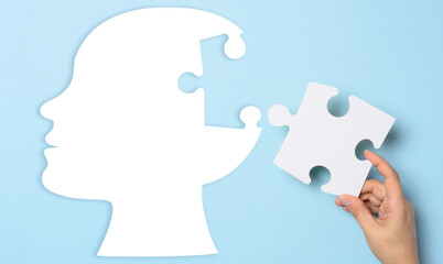 Silhouette of a human head holding a puzzle piece on a blue background, representing mental health