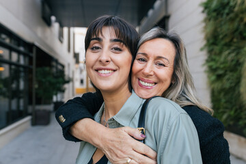 Smiling mature woman hugging friend from behind in city