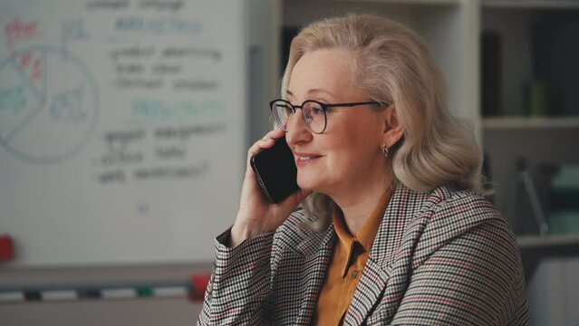 Beautiful middle-aged businesswoman smiling pleasantly while talking on phone