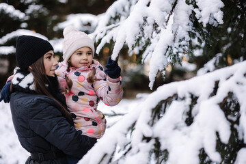 Happy mom and daughter shake off the snow from a Christmas tree branch
