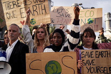 Multiethnic group of people at a refinery protesting against global warming, raising fist in favor...