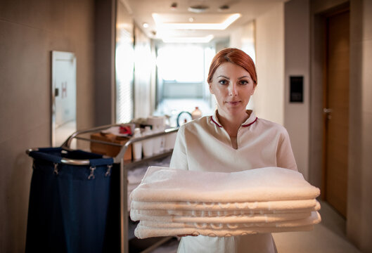 Woman housekeeper chambermaid holding fresh towels in hotel hallway looking at camera