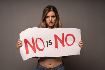 Determined woman holding a sign with 'NO is NO' during a protest for gender equality and human...