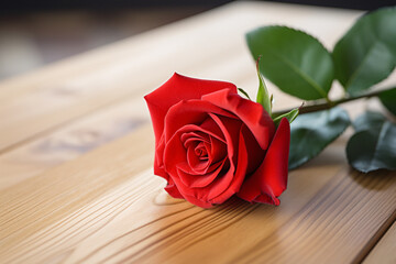 Beautiful red rose with soft petals and lush leaves on a light wooden table. Valentine's Day composition. A classic symbol for love. Perfect for romantic greetings, invitations, or banners