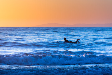 Sunset surfer on a blue ocean with golden sky and mountains, San Clemente Beach, California