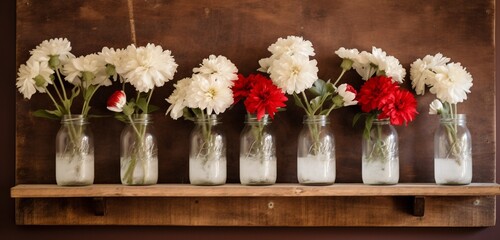 A rustic wooden shelf with mason jar vases filled with red and white flowers.