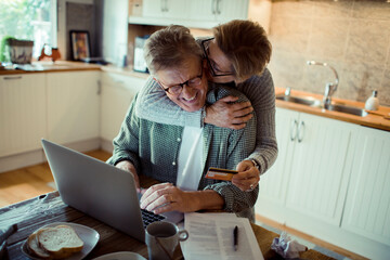 Mature middle aged senior couple online shopping from laptop at home