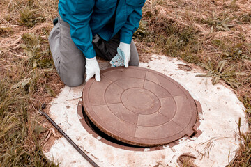 A worker lifts the manhole cover on a well for inspection and maintenance. Plumbing work in rural...