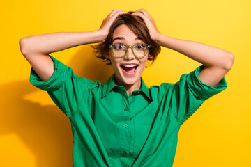 Photo of excited cheerful lady wear green shirt spectacles arms hands head open mouth isolated yellow color background