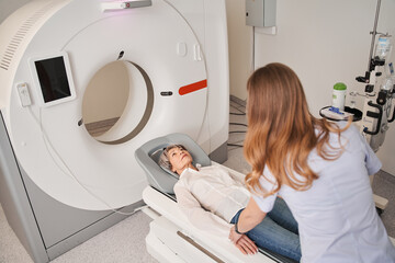 Mature female patient lies on CT or MRI bed moved inside the machine