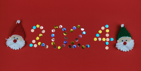 Happy new year 2024 red background. Round multicolored sequins. Minimalistic Christmas greeting card. Toy amigurumi Santa Claus head.