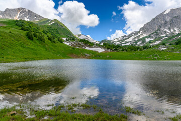 Lake in the Alpine mountains with mountains, green grassy meadows in springtime.