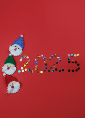 Happy new year 2025 red vertical background with copy space. Round multicolored sequins. Minimalistic Christmas greeting card. Toy amigurumi Santa Claus head.