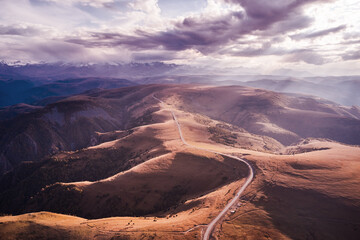 Fototapeta premium Panoramic view of the road winding along the mountain plateau. Autumn. Cloudy day. Shooting from a drone.