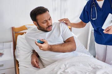 Obraz premium african american nurse helping her indian patient with asthma inhaler in his hospital ward