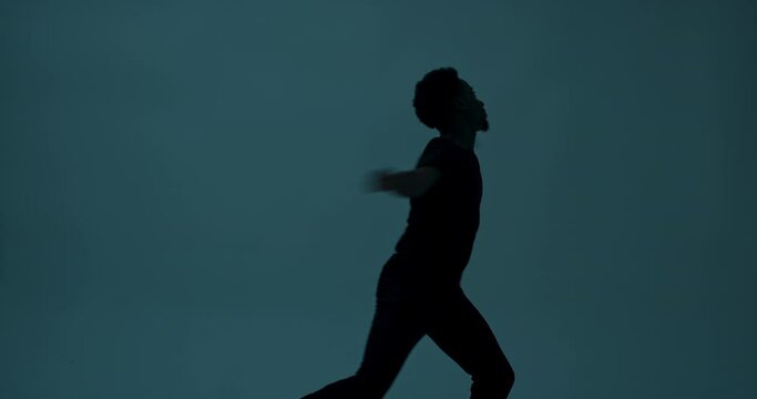 Plain dark studio with light dark skinned atractive young man in plaing casual black t-shirt standing in studio isolated dancing catching light showing different body movements.