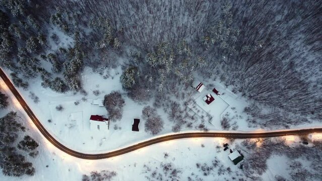 Amazing evening aerial view from drone on road between scenic mountains in winter. Top-down view of a picturesque mountain serpentine and cozy snow-covered houses. Magic winter landscape