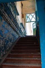 An old abandoned red wooden staircase in a crumbling building with blue walls and a beautiful window