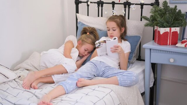 A girl reads a book for her younger sister before going to bed lying in the same bed.