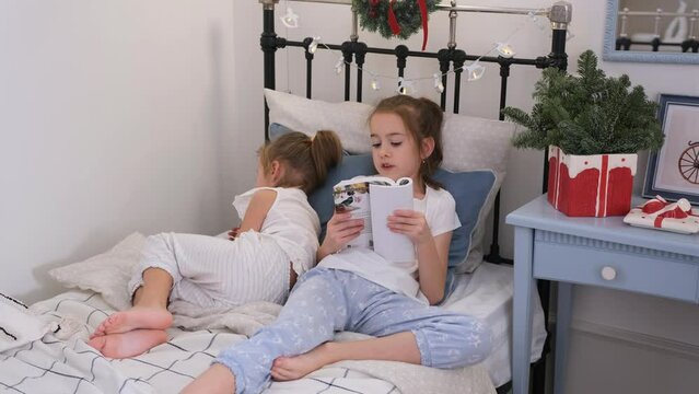 A girl reads a book for her younger sister before going to bed lying in the same bed.