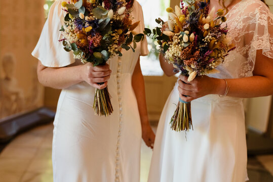 Two lesbian women are getting married, dressed as brides and holding a bouquet.