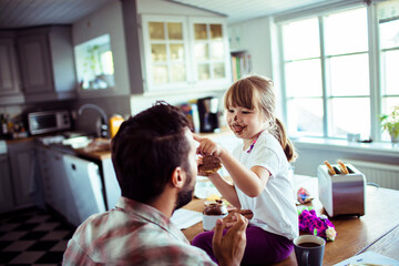 Father and Daughter Playing with Food in the Kitchen. Little girl putting chocolate on dad face...