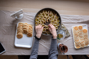 Hands holding Qatayef filled with chocolate and topped with pistachios on a wooden table, with a...