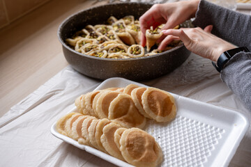 Hands holding Qatayef filled with chocolate and topped with pistachios on a wooden table, with a plate to be prepared in the oven later as Ramadan sweets.