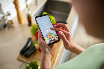 Young woman using recipe app on smartphone for preparing meal at home