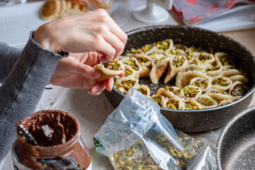 Hands holding Qatayef filled with chocolate and topped with pistachios on a wooden table, with a plate to be prepared in the oven later as Ramadan sweets.