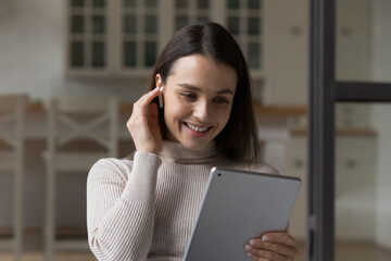 Beautiful young woman wear wireless earphones use digital tablet at home, close up, spend time on internet, watch video vlog, enjoy videocall talks via application. Modern tech, fun, leisure concept