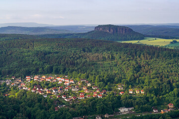 The light falls beautifully on a small town in a valley among the majestic mountains in the Saxon Switzerland National Park. Mount Pfaffenstein is in the background.
