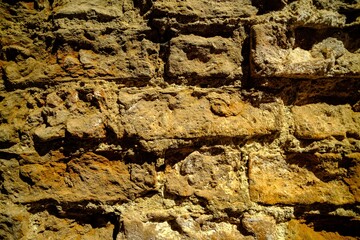Close-up outdoor view of part of an ancient stone wall with a textured surface. An abstract image of a brown cemented, durable facade.